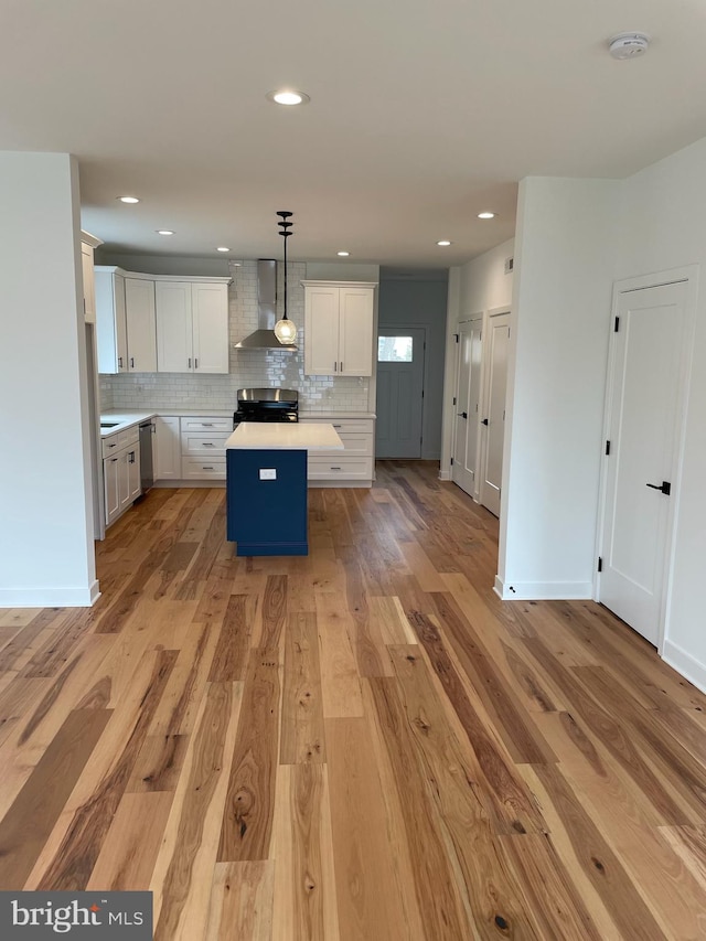 kitchen with appliances with stainless steel finishes, light wood-type flooring, wall chimney exhaust hood, white cabinets, and hanging light fixtures