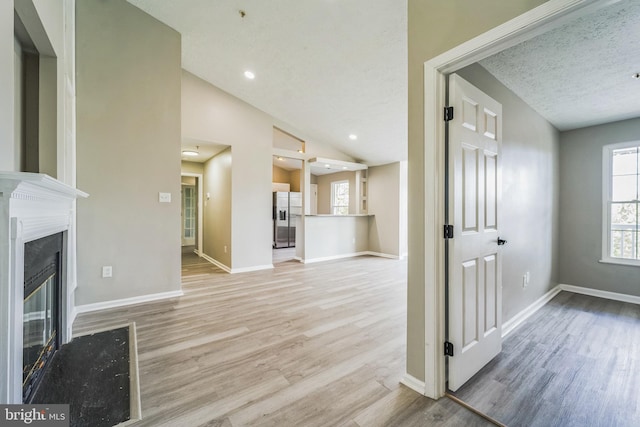 unfurnished living room featuring light hardwood / wood-style floors, a textured ceiling, and lofted ceiling