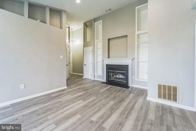 unfurnished living room with built in features, a textured ceiling, and light wood-type flooring