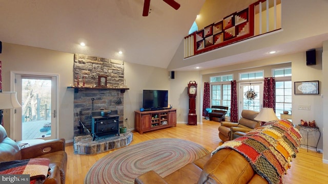 living room with baseboards, ceiling fan, wood finished floors, a wood stove, and high vaulted ceiling