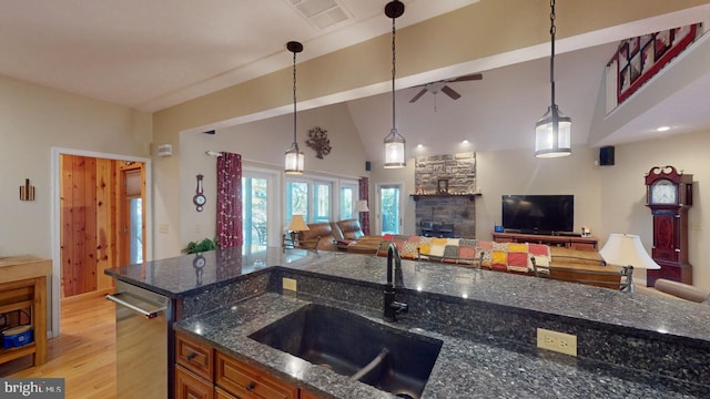 kitchen featuring open floor plan, a sink, a stone fireplace, and dishwasher