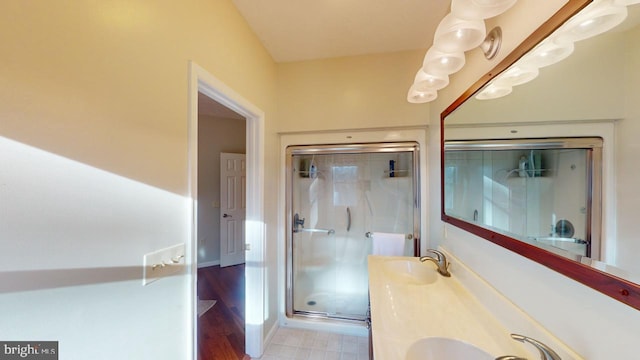 bathroom with double vanity, a shower stall, baseboards, and a sink