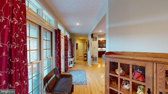 hall featuring light wood finished floors, visible vents, and a textured ceiling