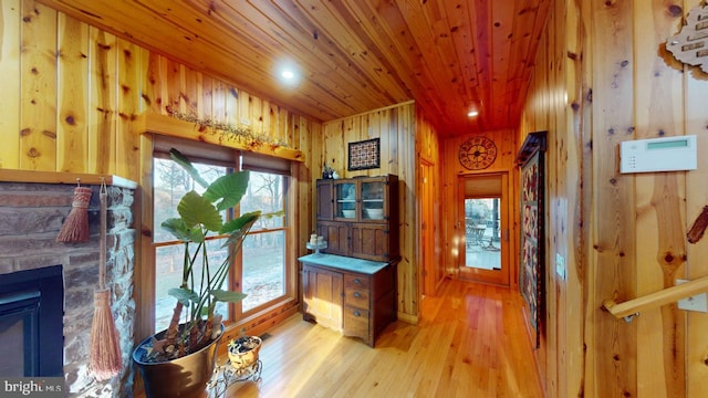 doorway featuring light wood-type flooring, wooden walls, wood ceiling, and a fireplace