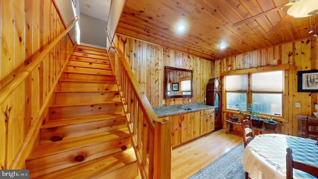 kitchen with light wood-type flooring, wood ceiling, a sink, and wooden walls