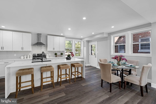 kitchen with wall chimney range hood, a center island with sink, dark hardwood / wood-style flooring, white cabinetry, and sink