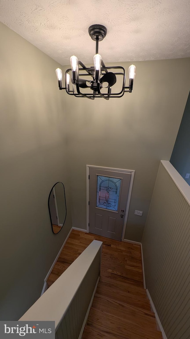 stairs featuring hardwood / wood-style floors, a textured ceiling, and an inviting chandelier