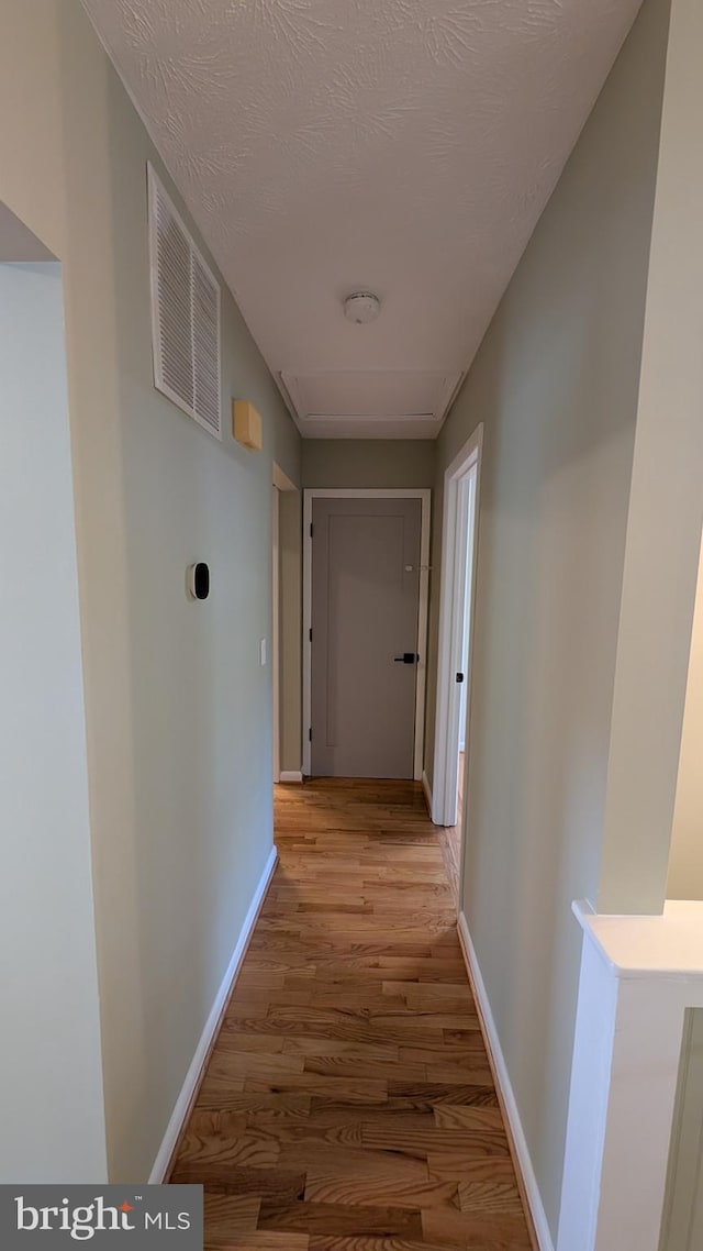 corridor with a textured ceiling and light hardwood / wood-style floors