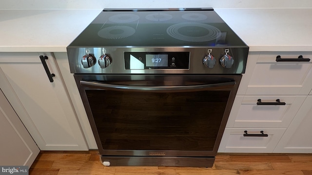 details with stainless steel range, white cabinets, and light hardwood / wood-style flooring