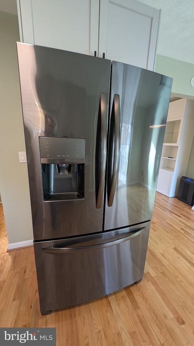 interior details featuring a textured ceiling, light hardwood / wood-style flooring, white cabinets, and stainless steel refrigerator with ice dispenser