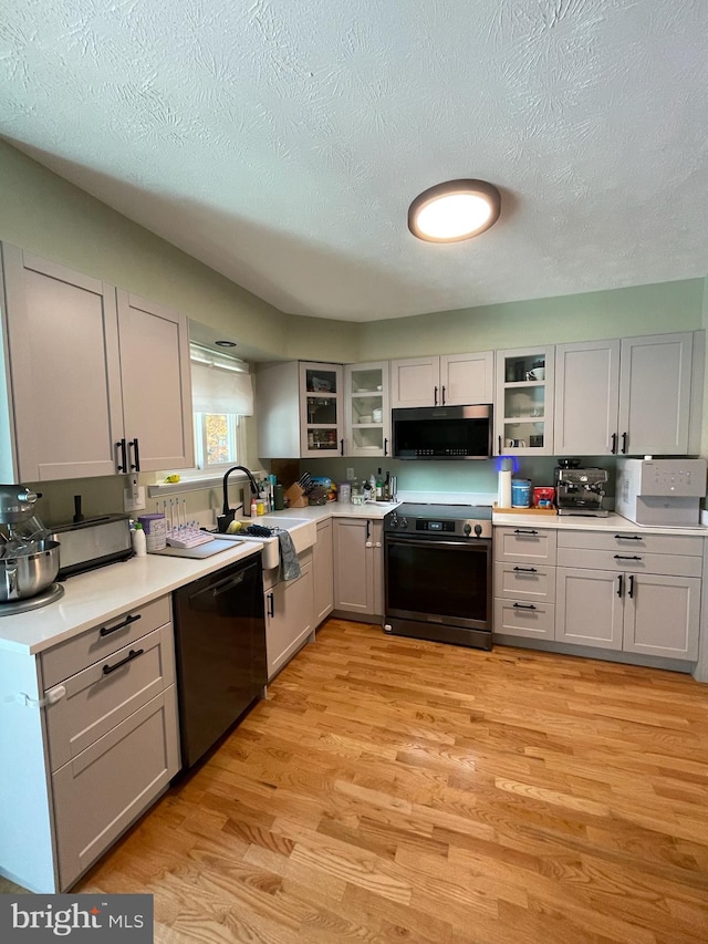 kitchen with sink, range with electric cooktop, light wood-type flooring, a textured ceiling, and black dishwasher