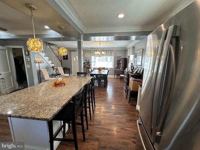 kitchen with dark wood-type flooring, hanging light fixtures, ornamental molding, stainless steel fridge, and a kitchen bar