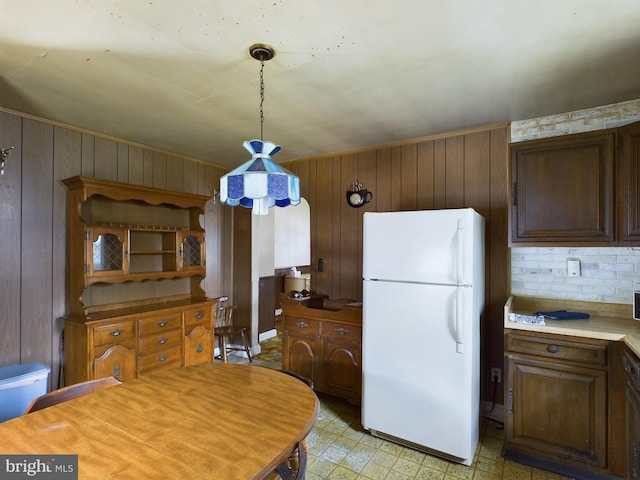 kitchen with wooden walls, tasteful backsplash, pendant lighting, and white refrigerator