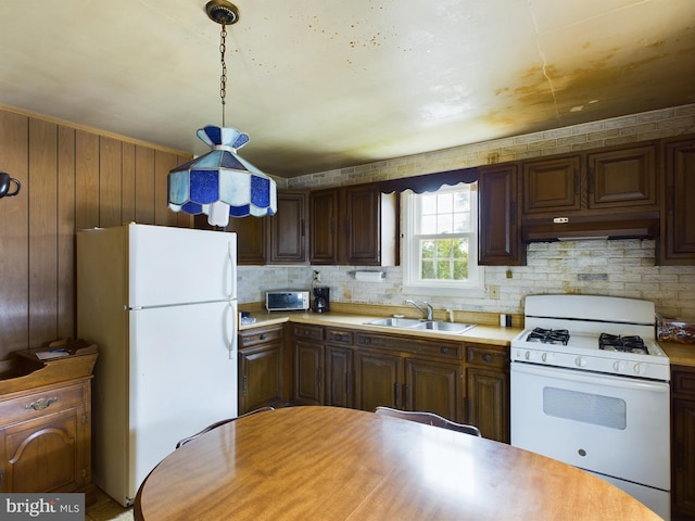 kitchen with white appliances, wood walls, tasteful backsplash, sink, and decorative light fixtures