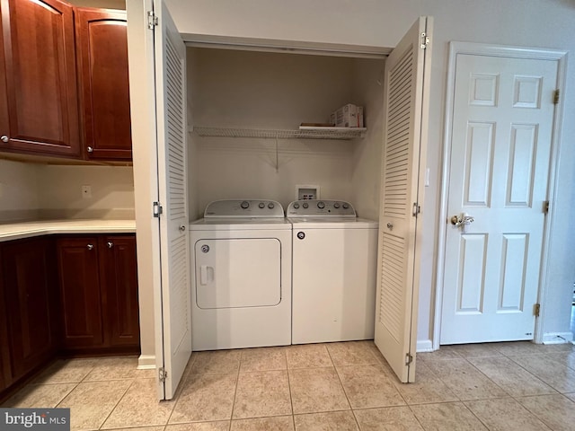 clothes washing area with cabinets, light tile patterned floors, and washing machine and clothes dryer