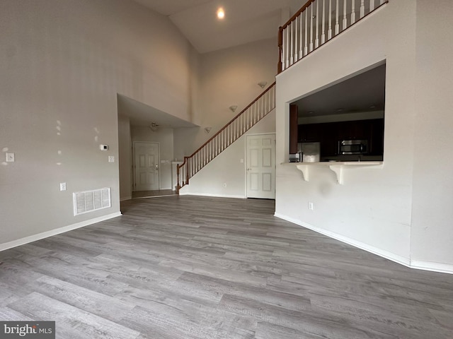 unfurnished living room with high vaulted ceiling and wood-type flooring