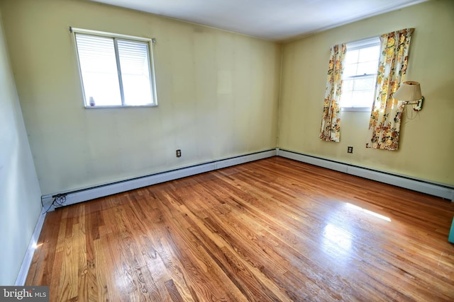 empty room with baseboards, a baseboard heating unit, and wood finished floors