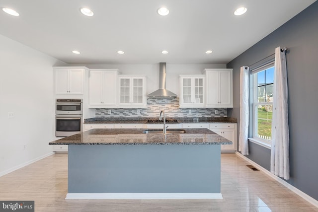 kitchen featuring wall chimney range hood, white cabinetry, appliances with stainless steel finishes, and plenty of natural light