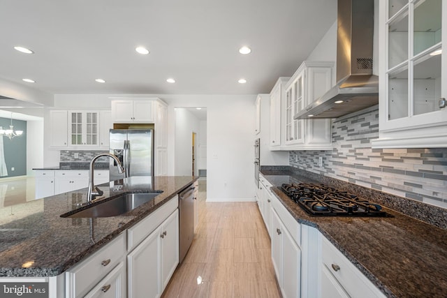 kitchen featuring white cabinets, appliances with stainless steel finishes, dark stone countertops, wall chimney exhaust hood, and sink