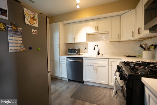 kitchen featuring sink, wood-type flooring, white cabinetry, appliances with stainless steel finishes, and decorative backsplash