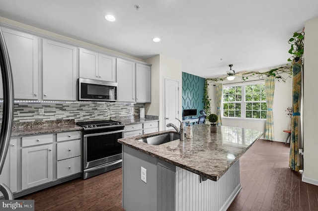 kitchen with light stone counters, stainless steel appliances, sink, dark hardwood / wood-style flooring, and a center island with sink