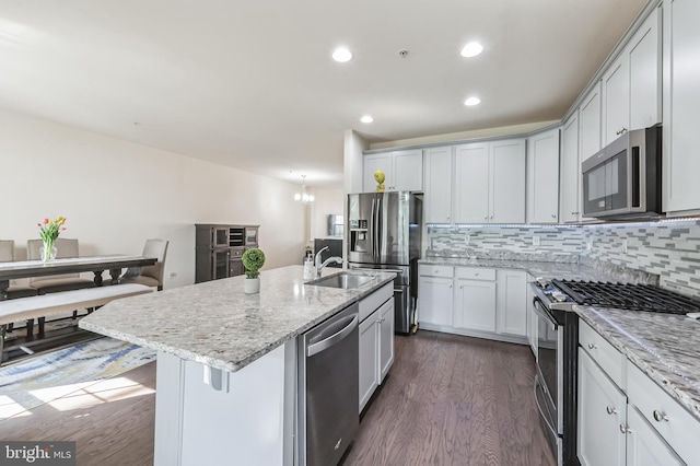 kitchen featuring light stone counters, a center island with sink, backsplash, stainless steel appliances, and dark hardwood / wood-style floors