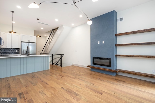 kitchen featuring backsplash, pendant lighting, white cabinetry, appliances with stainless steel finishes, and light hardwood / wood-style floors