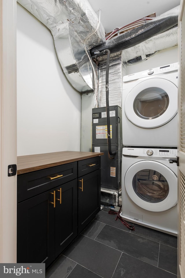 clothes washing area featuring dark tile patterned floors, stacked washer / drying machine, and cabinets