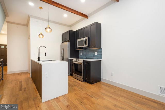 kitchen with appliances with stainless steel finishes, a kitchen island with sink, light wood-type flooring, sink, and decorative light fixtures