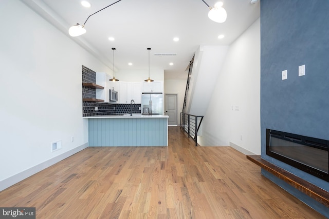 kitchen with light wood-type flooring, kitchen peninsula, stainless steel appliances, pendant lighting, and white cabinets