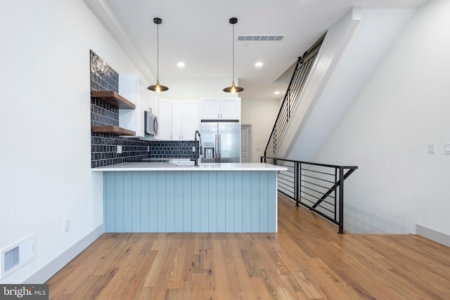 kitchen featuring kitchen peninsula, appliances with stainless steel finishes, white cabinetry, light wood-type flooring, and pendant lighting