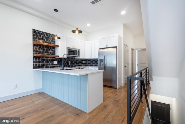 kitchen with kitchen peninsula, white cabinets, pendant lighting, light wood-type flooring, and appliances with stainless steel finishes