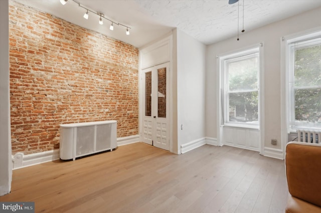 interior space featuring light hardwood / wood-style flooring, radiator heating unit, and brick wall