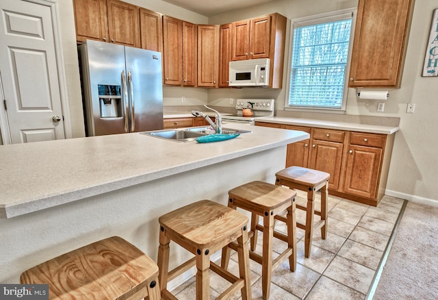 kitchen with white appliances, sink, light tile patterned floors, and a breakfast bar area