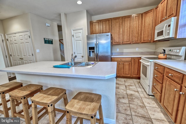 kitchen with a kitchen bar, white appliances, sink, and a kitchen island with sink