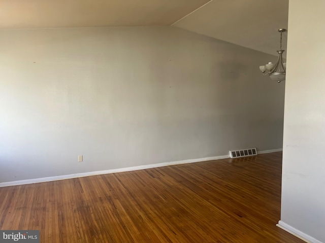 spare room with an inviting chandelier, dark wood-type flooring, and vaulted ceiling