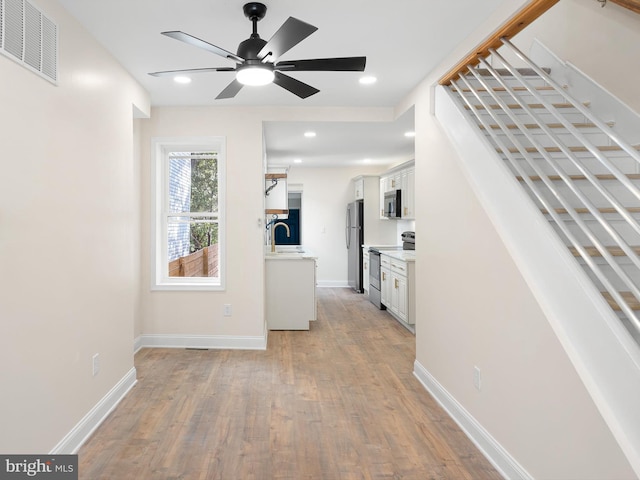 interior space featuring ceiling fan, appliances with stainless steel finishes, white cabinetry, light hardwood / wood-style flooring, and sink