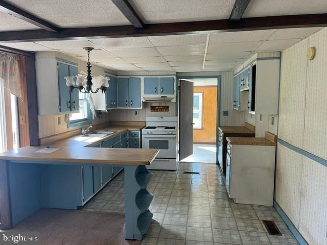 kitchen with kitchen peninsula, blue cabinets, white stove, sink, and decorative light fixtures