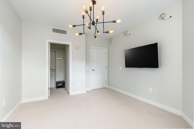 unfurnished bedroom featuring a spacious closet, a closet, light colored carpet, and an inviting chandelier