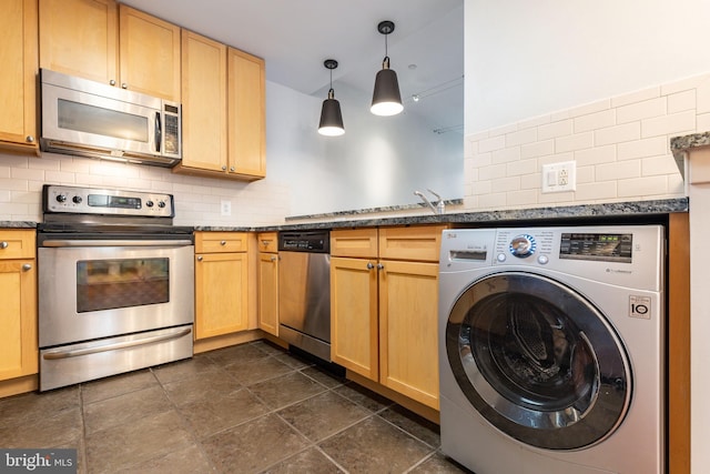 kitchen with pendant lighting, dark tile patterned flooring, stainless steel appliances, washer / dryer, and decorative backsplash