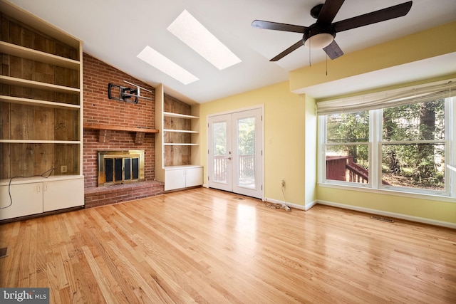 unfurnished living room featuring vaulted ceiling with skylight, a fireplace, light hardwood / wood-style floors, and ceiling fan