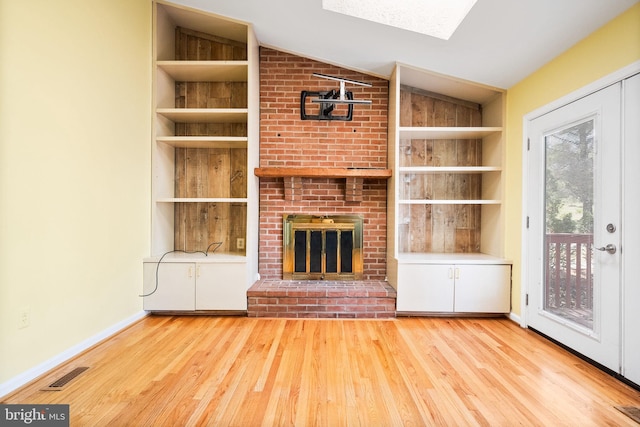 unfurnished living room with built in shelves, light wood-type flooring, and vaulted ceiling