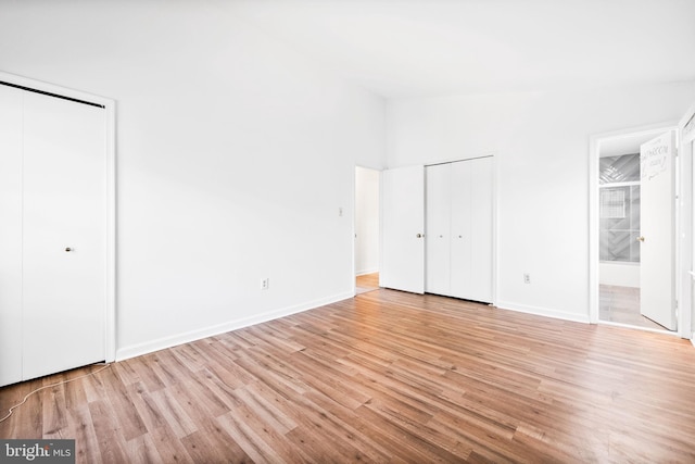 unfurnished bedroom with ensuite bath, light wood-type flooring, and two closets