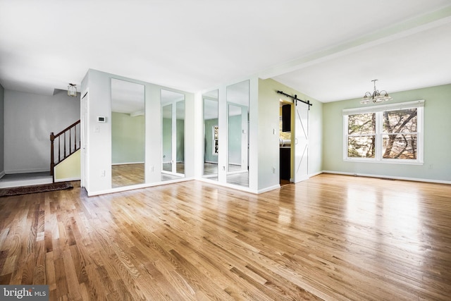 unfurnished living room with light hardwood / wood-style floors, a barn door, and a chandelier