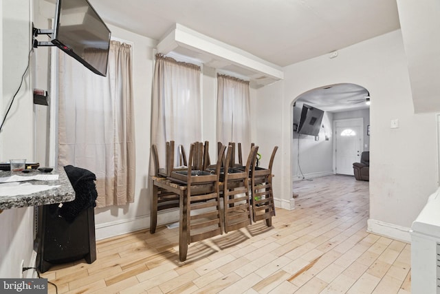 dining room featuring baseboards, a ceiling fan, arched walkways, and wood finished floors