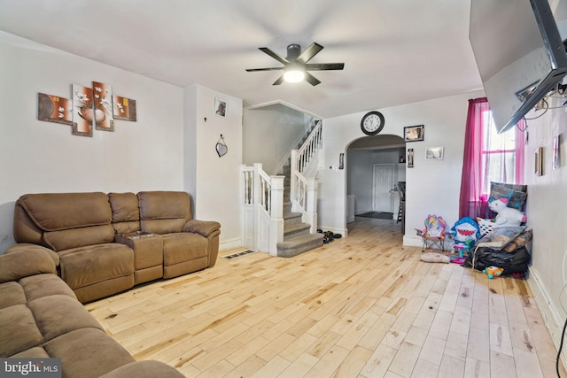 living area featuring arched walkways, wood finished floors, ceiling fan, and stairs