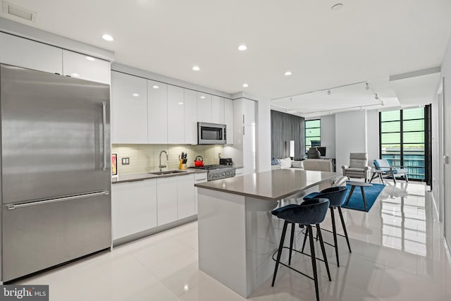 kitchen featuring stainless steel appliances, a sink, modern cabinets, a breakfast bar area, and white cabinetry