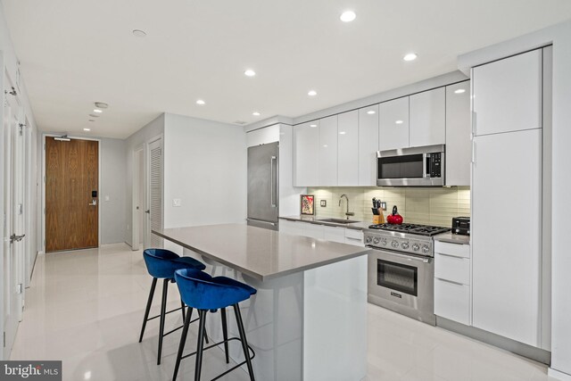 kitchen featuring white cabinets, a sink, a kitchen bar, modern cabinets, and high quality appliances