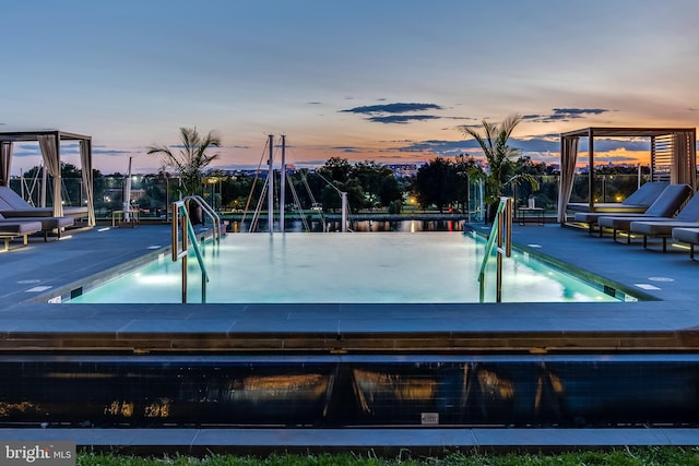 pool at dusk featuring a patio and a hot tub