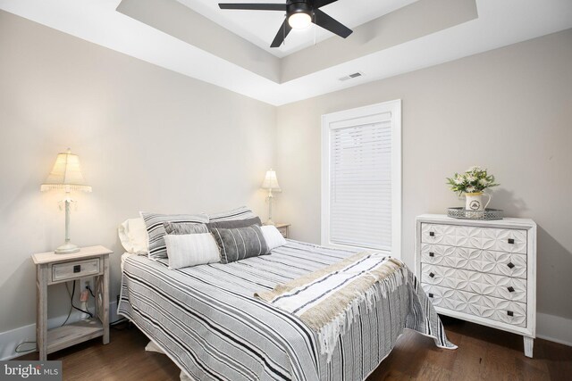 bedroom featuring dark wood-type flooring, a tray ceiling, and ceiling fan